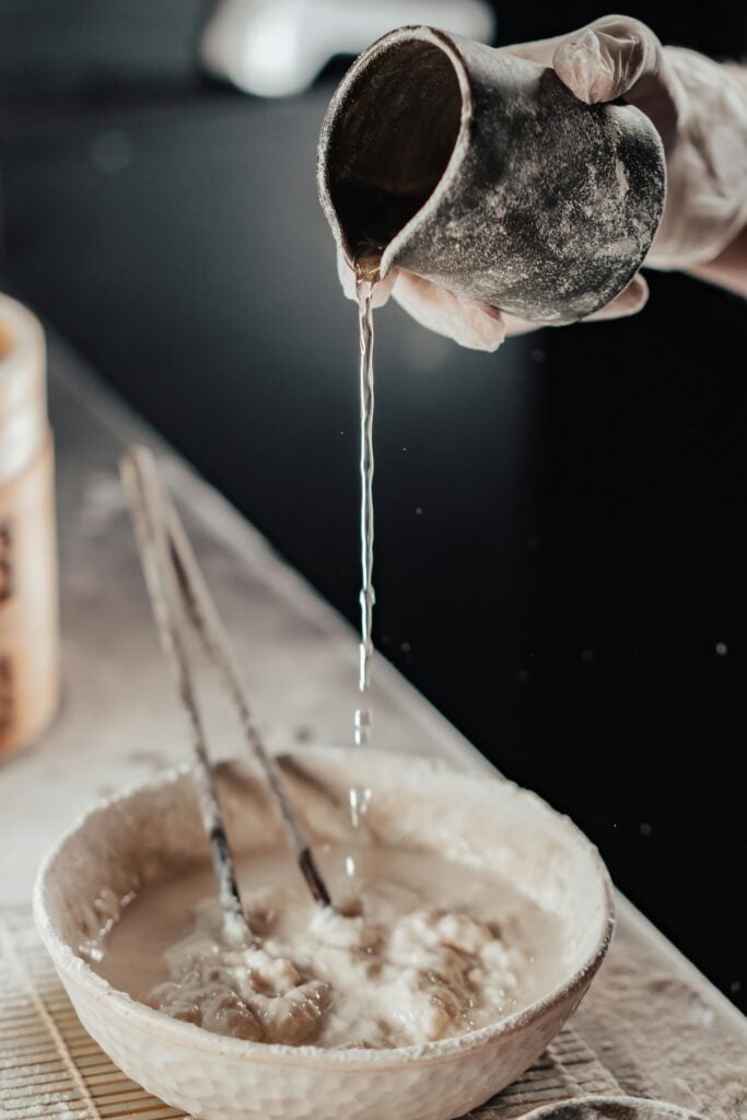Someone pouring water from a jar into a bowl to mix bread.