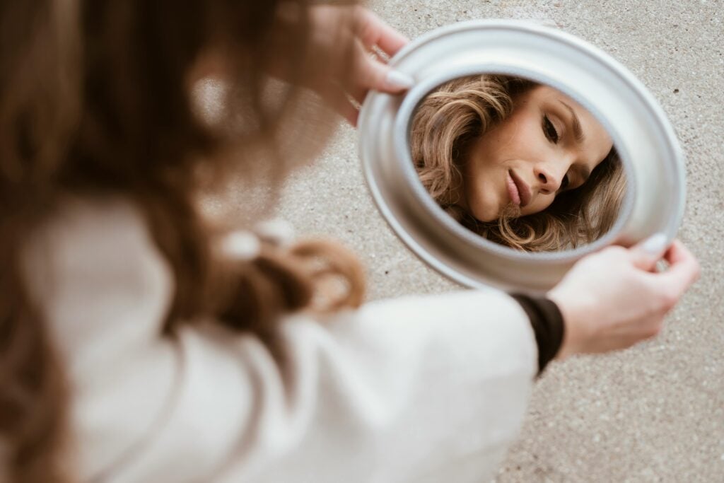 A woman looking down into a mirror at her reflection.