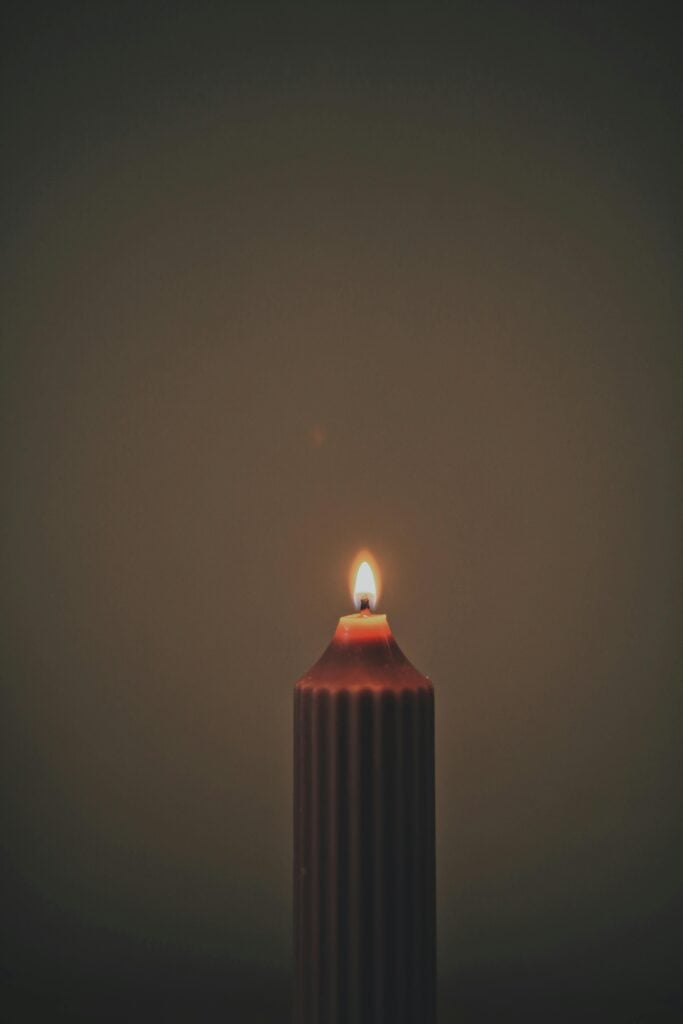 A single candle in front of a dark grey background.