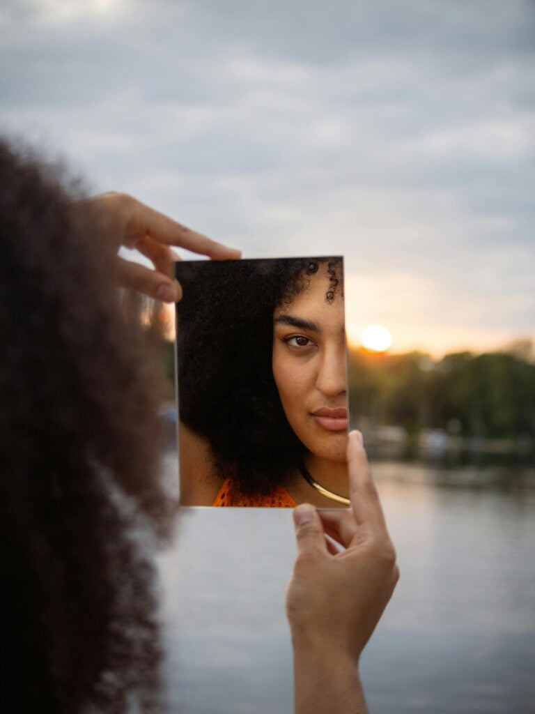 A woman holding a mirror and looking at her reflection.