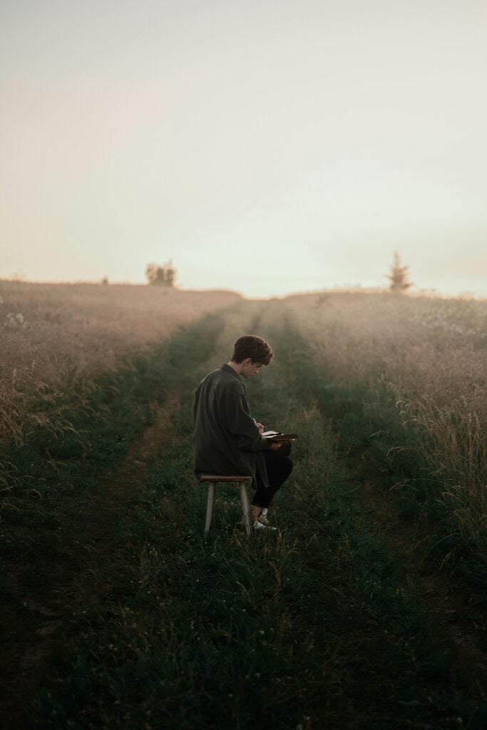 Someone sitting on a field of grass on a chair writing in a book.