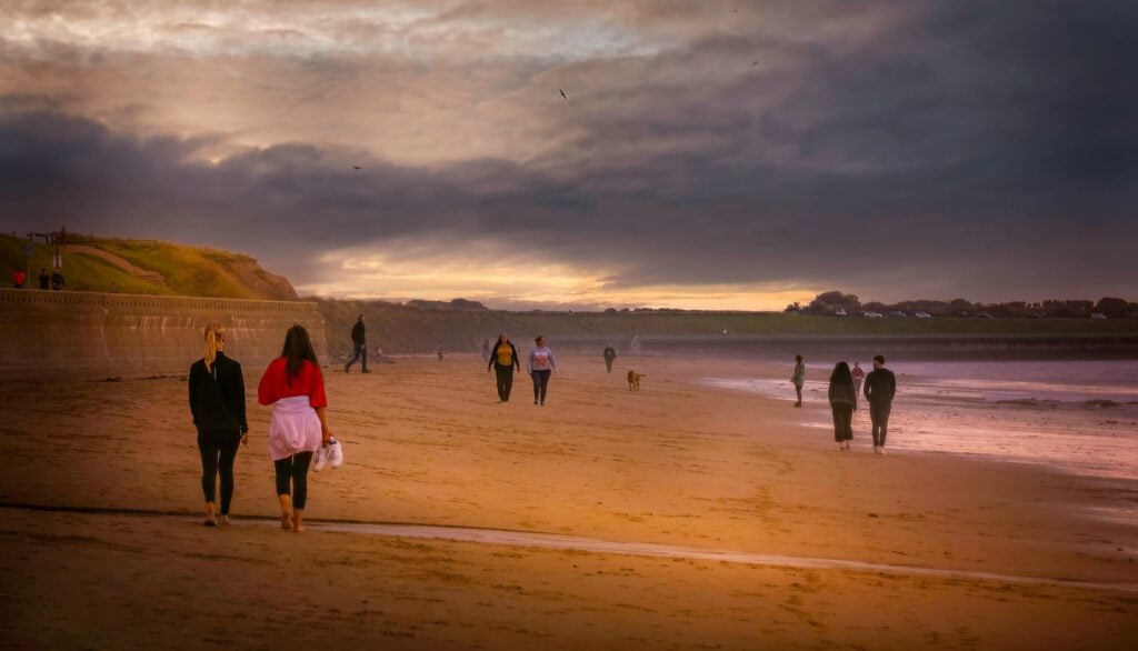 Group of people separated in pairs while walking on a beach.