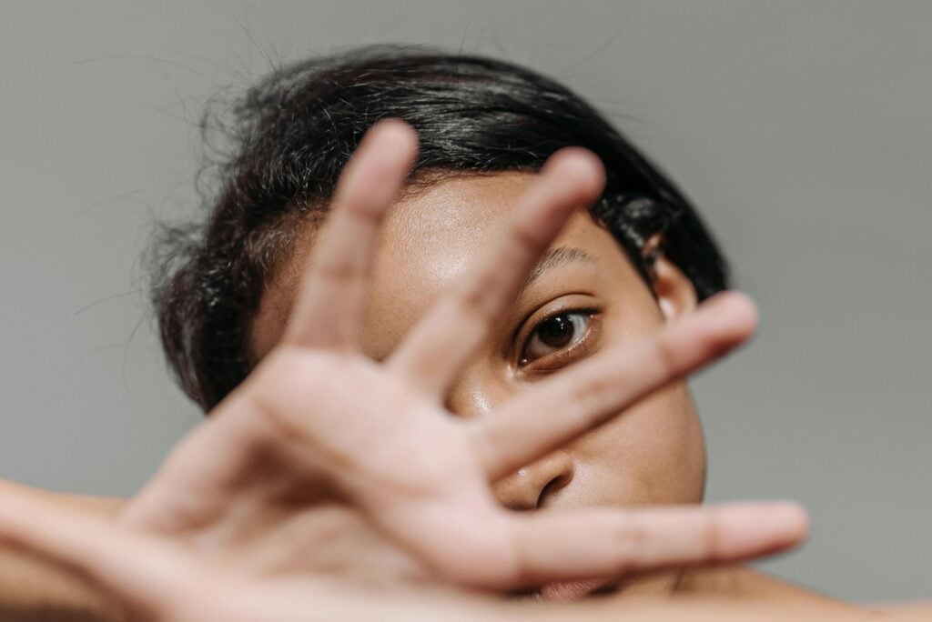 A woman looking forward with hand in front of face.