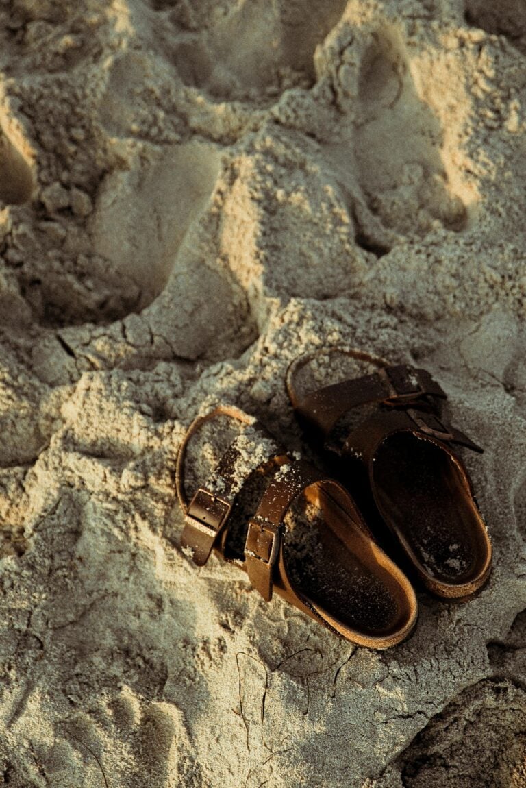 Sandals in sand with footprints.