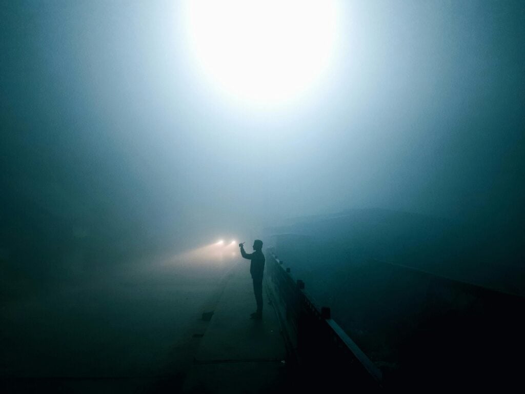 Someone standing in dark misty area with a light.