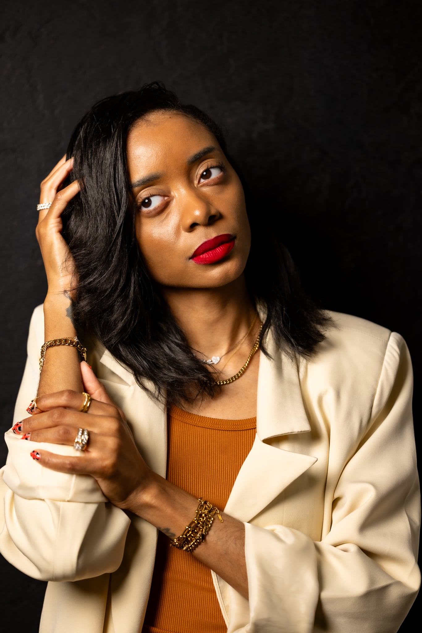 Shanika looking to the side slightly with hand holding head with a beige blazer and brown shirt.