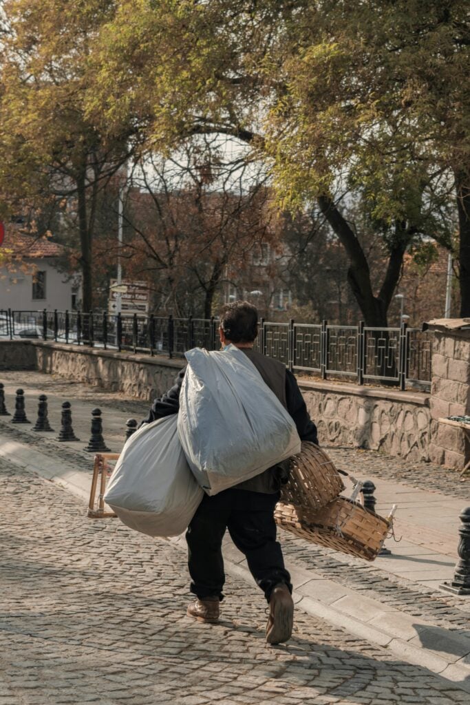 A man carrying two large bags while walking on a road.