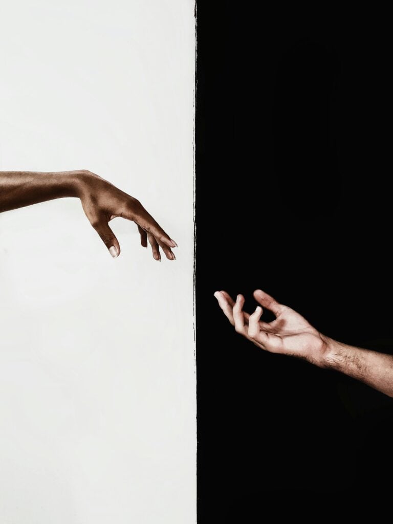 Two hands trying to grasp each other with a split black and white background.