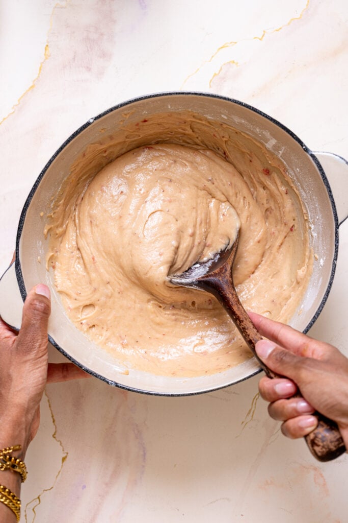 Cake batter in a bowl being stirred with woman hands.