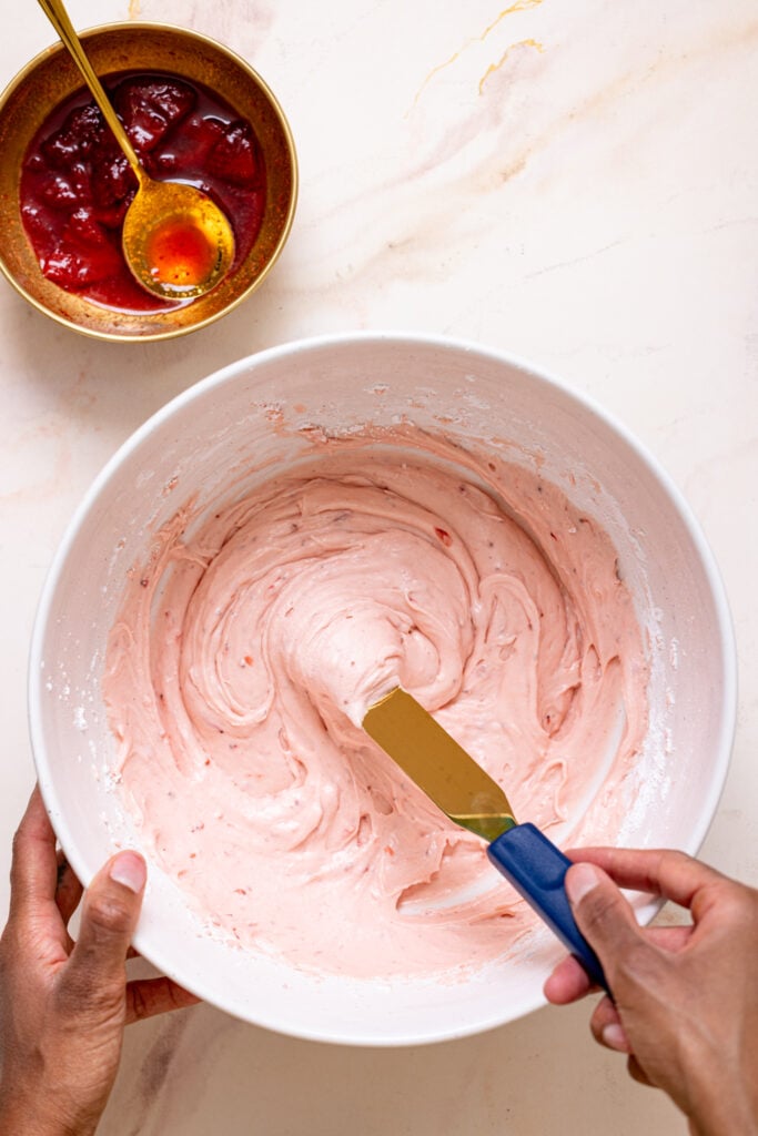 Strawberry frosting in a bowl being mixed with a spatula.