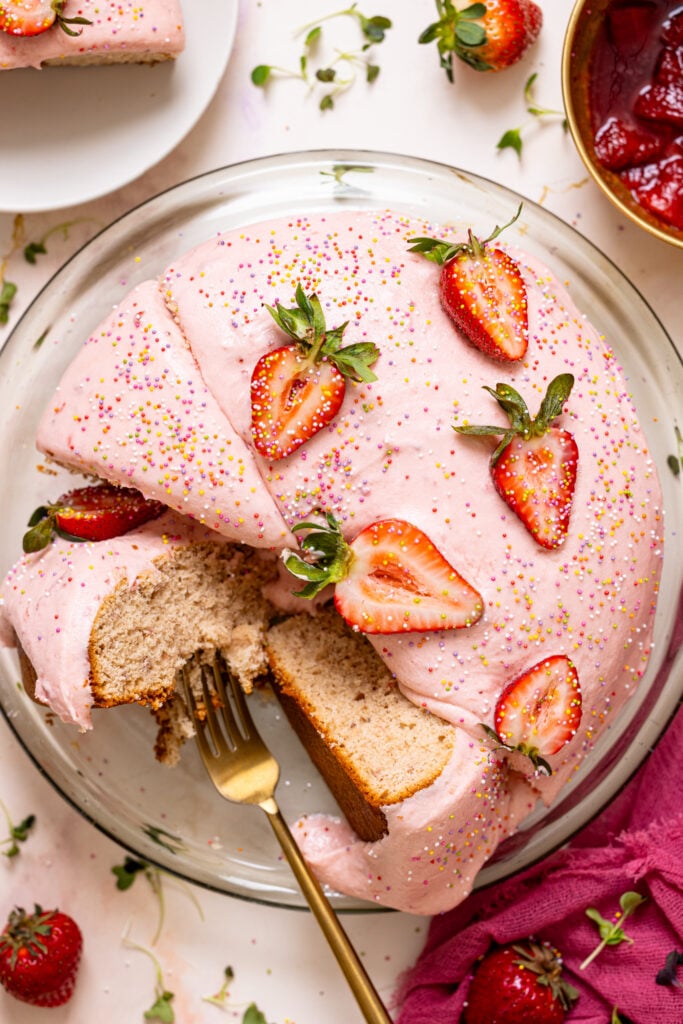 Strawberry cake on a cake stand sliced with fresh berries.