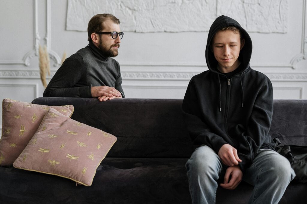 A guy and young man sitting on a couch looking unhappy.