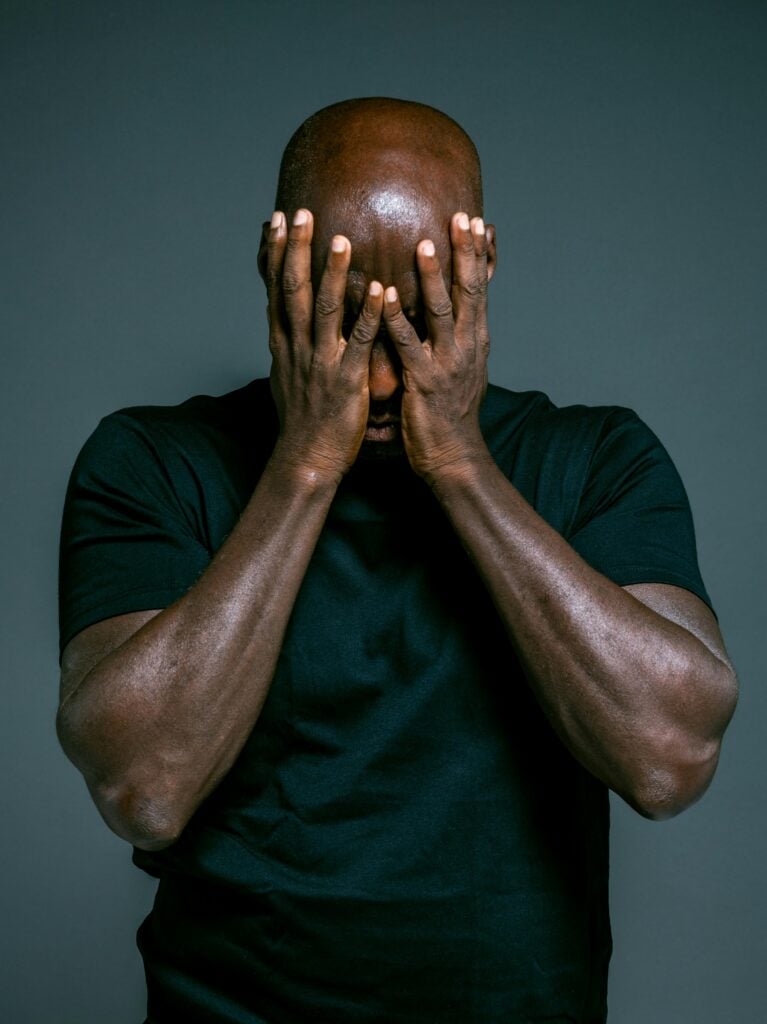 A guy in a dark blue shirt with hands over face in despair. 