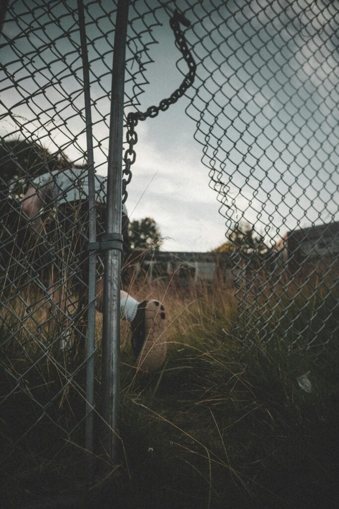 A broken fence with someone running through a field.