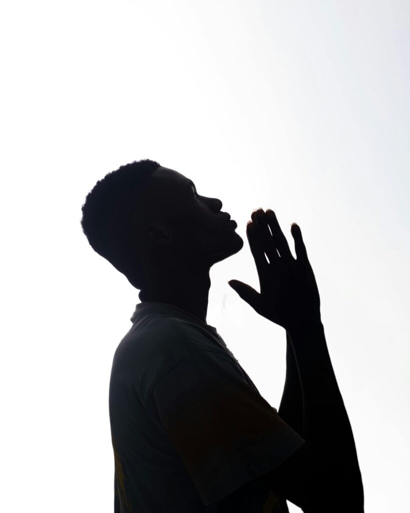 A person in black and white image looking up with praying hands.
