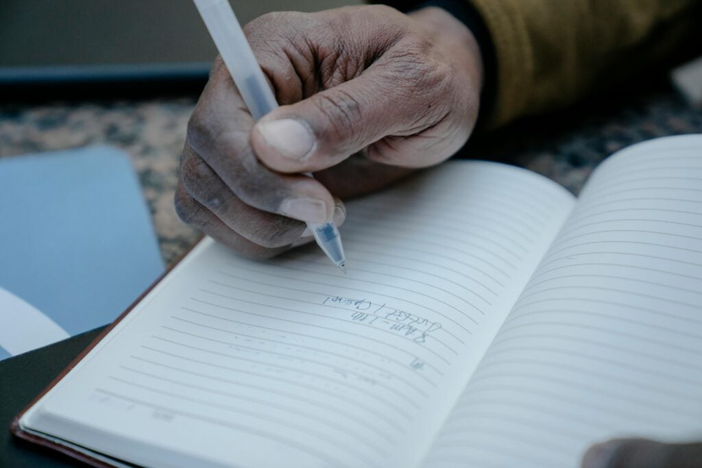 A man's hand writing in a notebook.