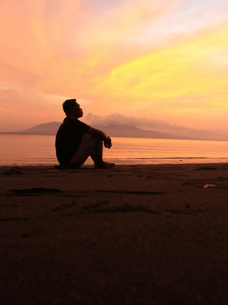 A man sitting on sand in front of a sunset.