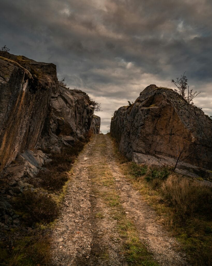 A narrow path with rocks on each side with grey skies.