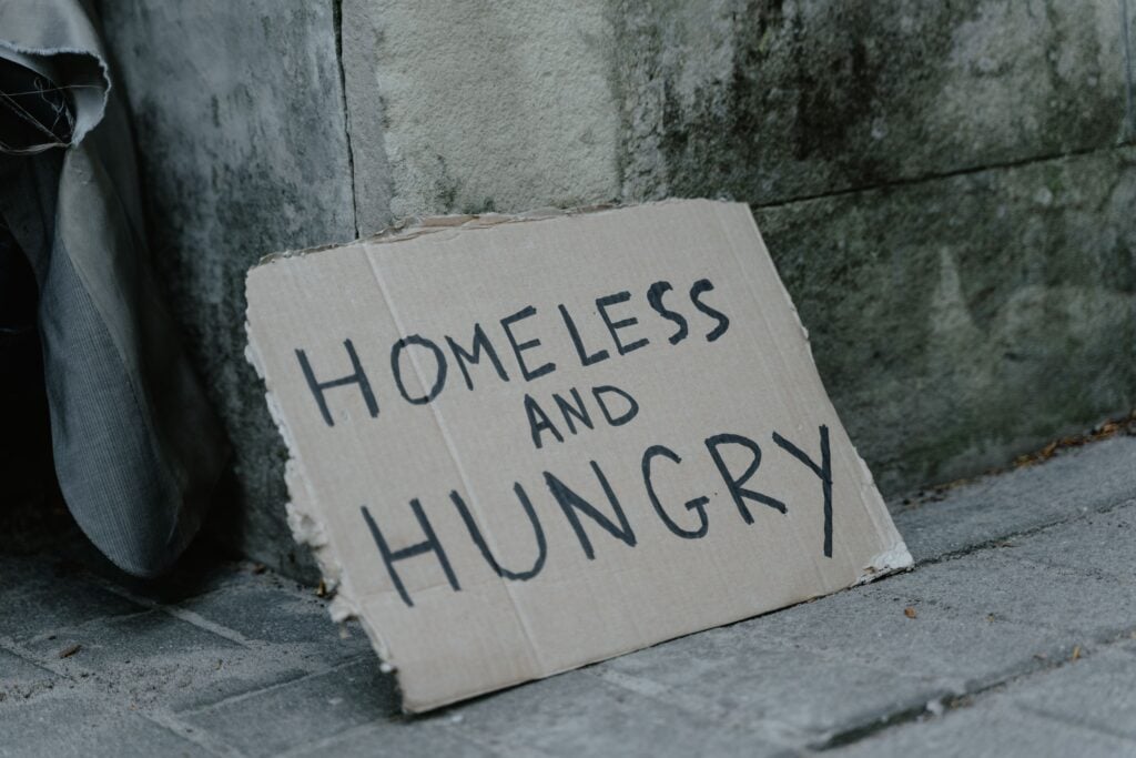 A cardboard sign that says Homeless and Hungry standing on the ground.