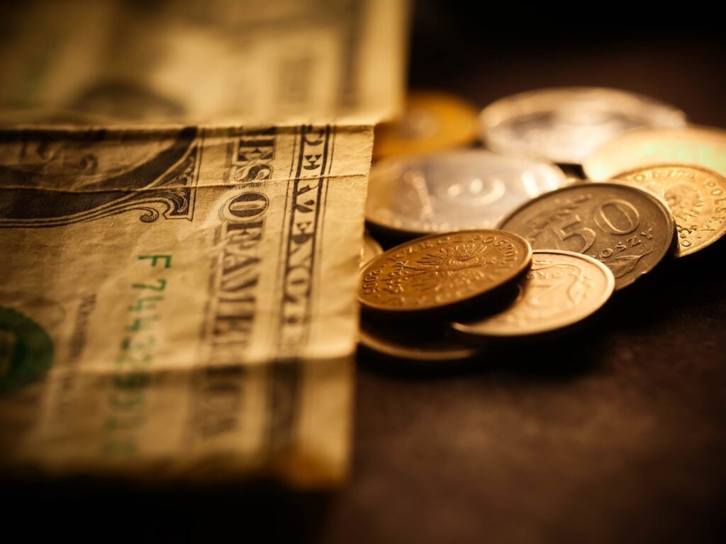 Dollar bills and coins on a table with a dark background.