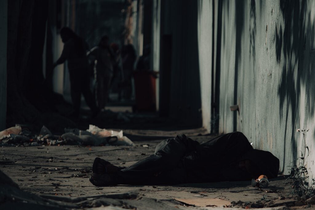 A homeless person laying on the ground outside. 