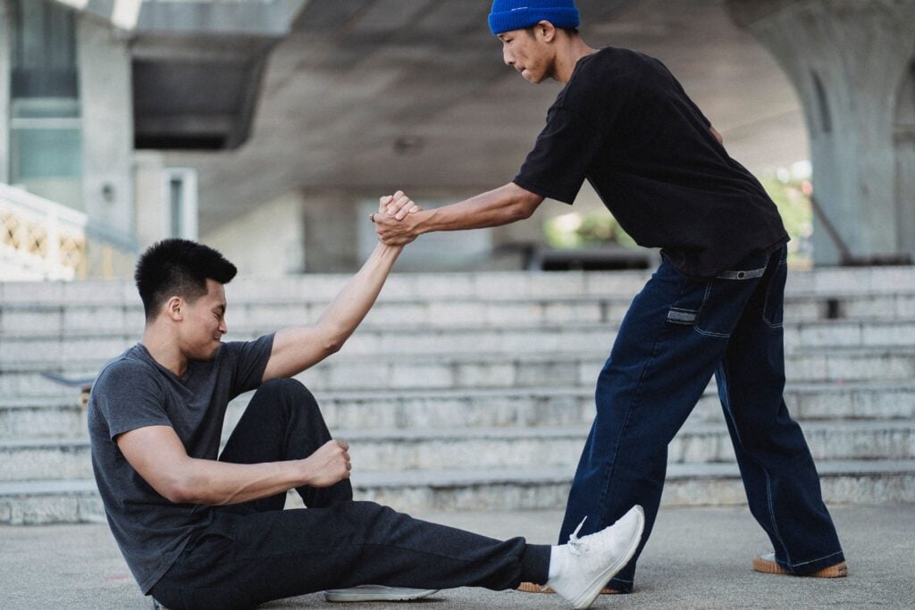 One guy helping up another guy from the ground.
