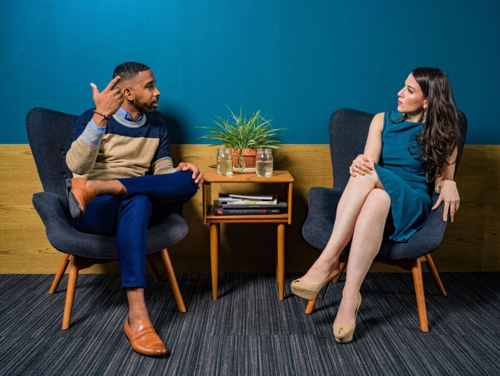 A black man and white woman having a serious conversation around a table.