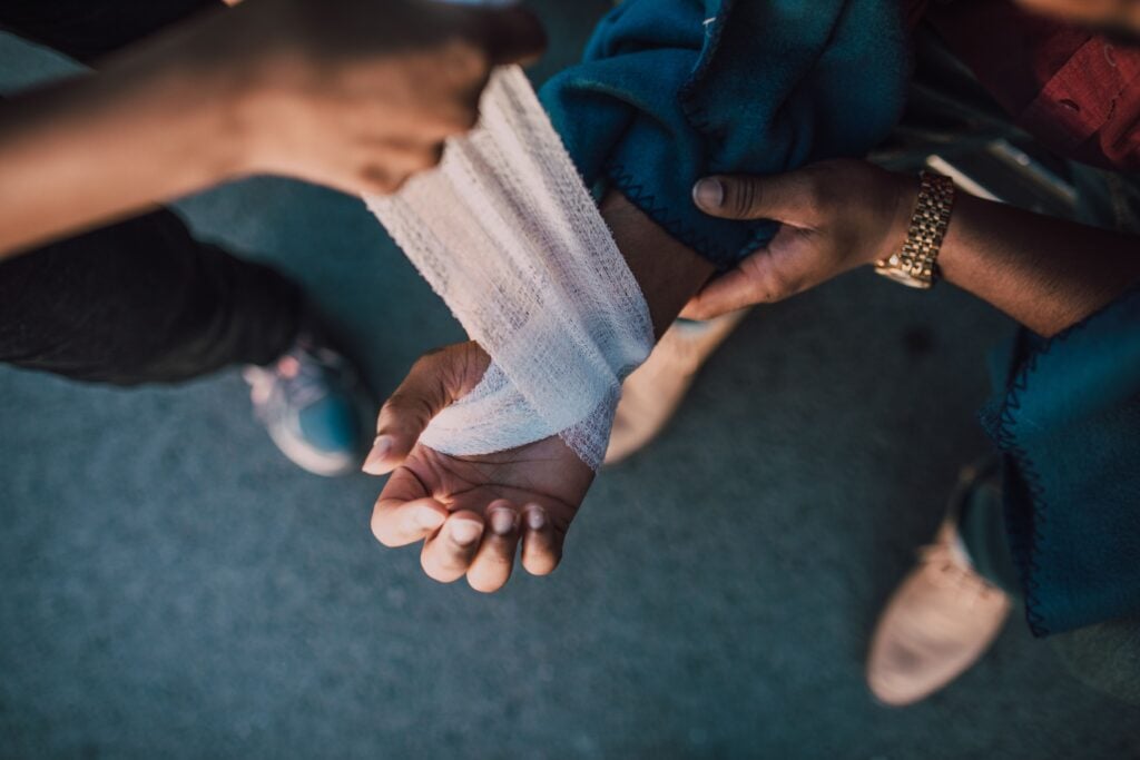 Someone putting on a bandage on another's hand that is wounded.